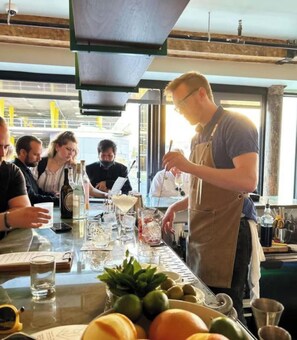 Uma área de bar com um bartender preparando bebidas, um menu e uma mesa com copos e garrafas.