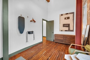 A room with wooden flooring, a door, a wall-mounted coat rack, a bench, and a painting.