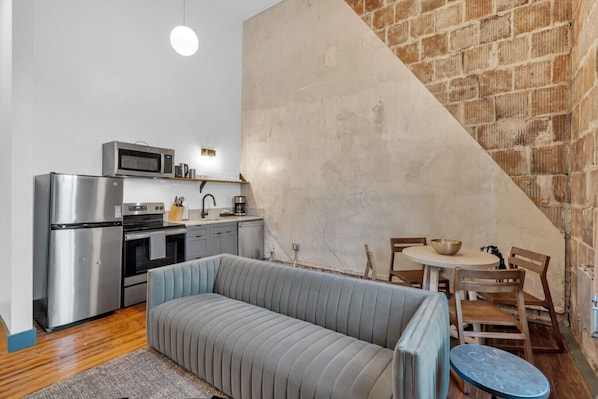 A compact kitchen with modern appliances, a dining area with a round table and chairs, and a sofa.
