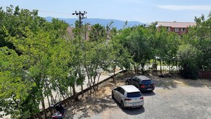 A parking area with two cars, surrounded by trees and a building with a red roof in the background. - TANGO PANSIYON (Koycegiz)