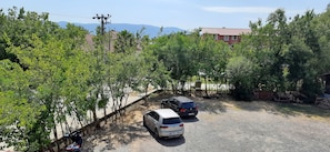 Un estacionamiento con dos coches, rodeado de árboles y un edificio de techo rojo al fondo.
