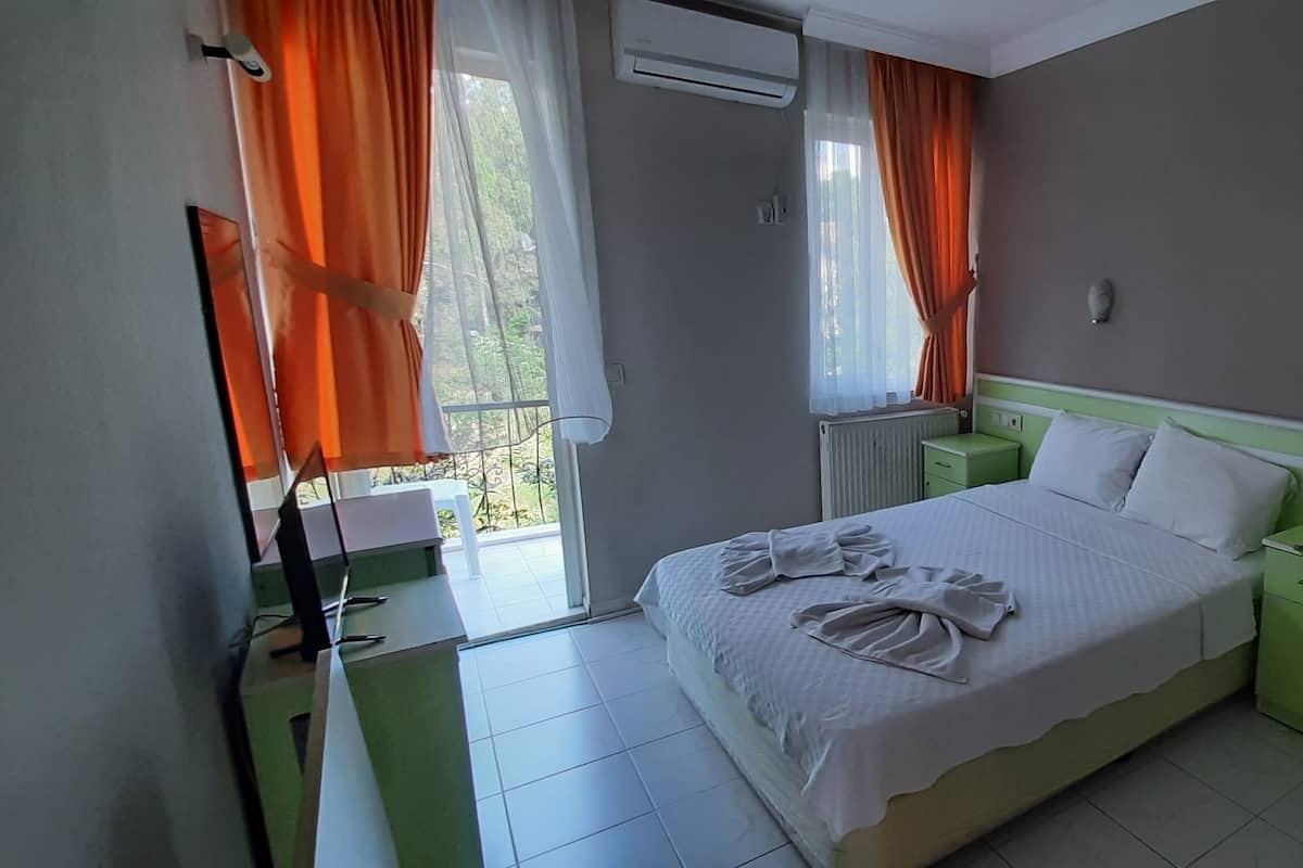Una habitación de hotel con cama, mesitas de noche verdes, un armario y una ventana con cortinas.