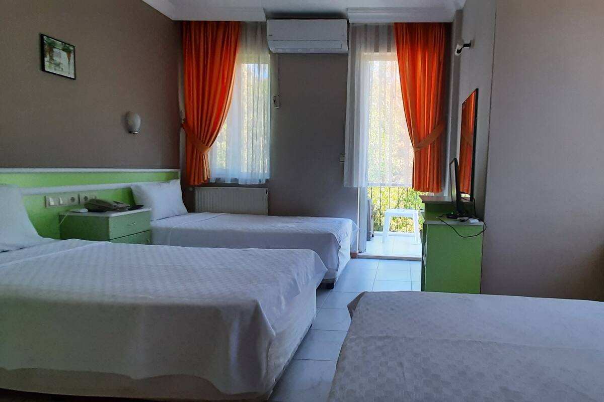 Habitación de hotel con dos camas, una mesita de noche verde, un aparador verde y una ventana con cortinas naranjas.
