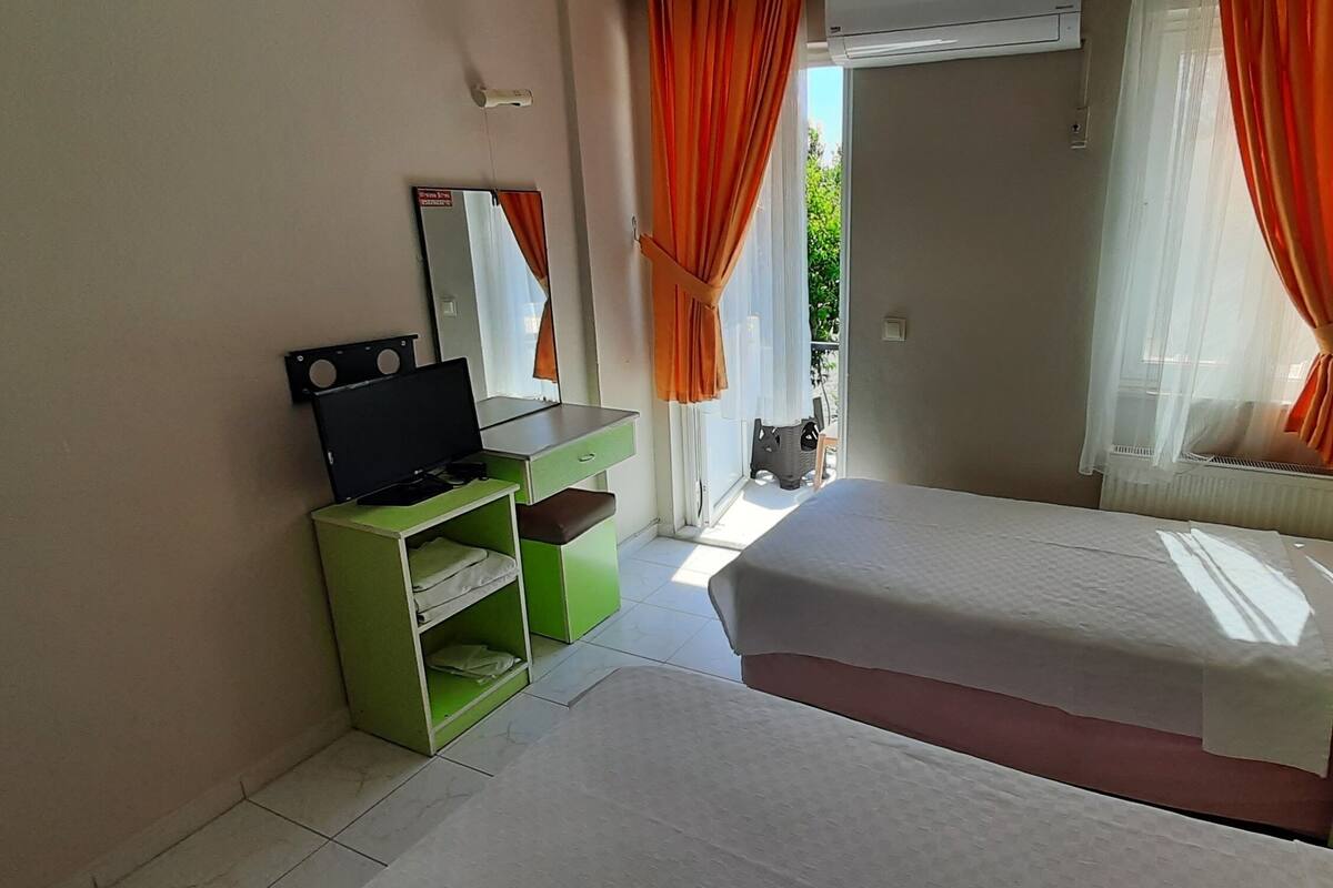 Habitación de hotel con dos camas, un escritorio con computadora, un espejo y una ventana con cortinas.