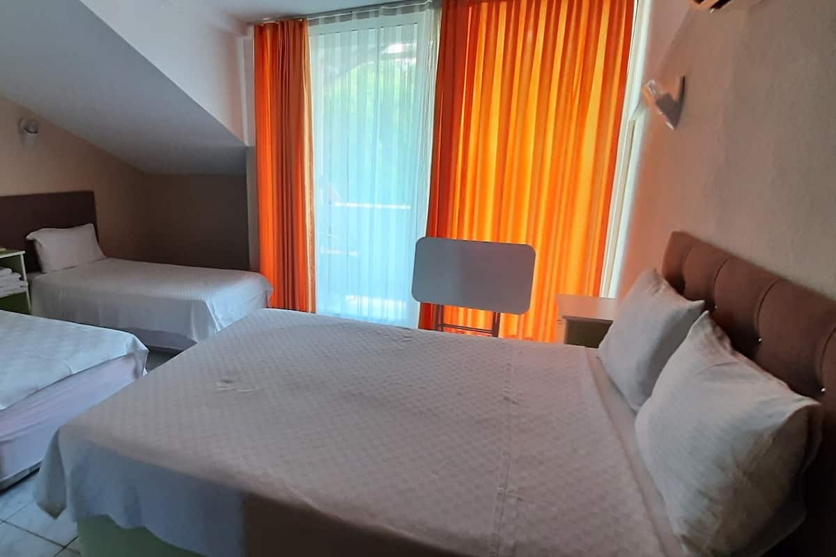 Habitación de hotel con dos camas, una mesita de noche, una lámpara y una ventana con cortinas.
