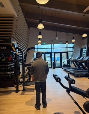 Ein Fitnessstudio mit Laufbändern, Kraftgeräten und einem großen Fenster.