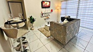A living room with a dining area, a sofa, a TV, and a window with blinds. - Elite Luxury Garden Escape, Executive Cottage in Welkom with Wi-Fi & Parking (Welkom)