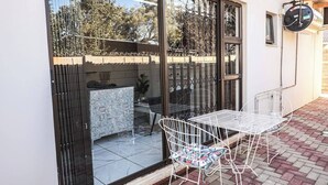 A patio with a table and chairs, a window with a view of the garden, and a water heater mounted on the wall. - Elite Luxury Garden Escape, Executive Cottage in Welkom with Wi-Fi & Parking (Welkom)