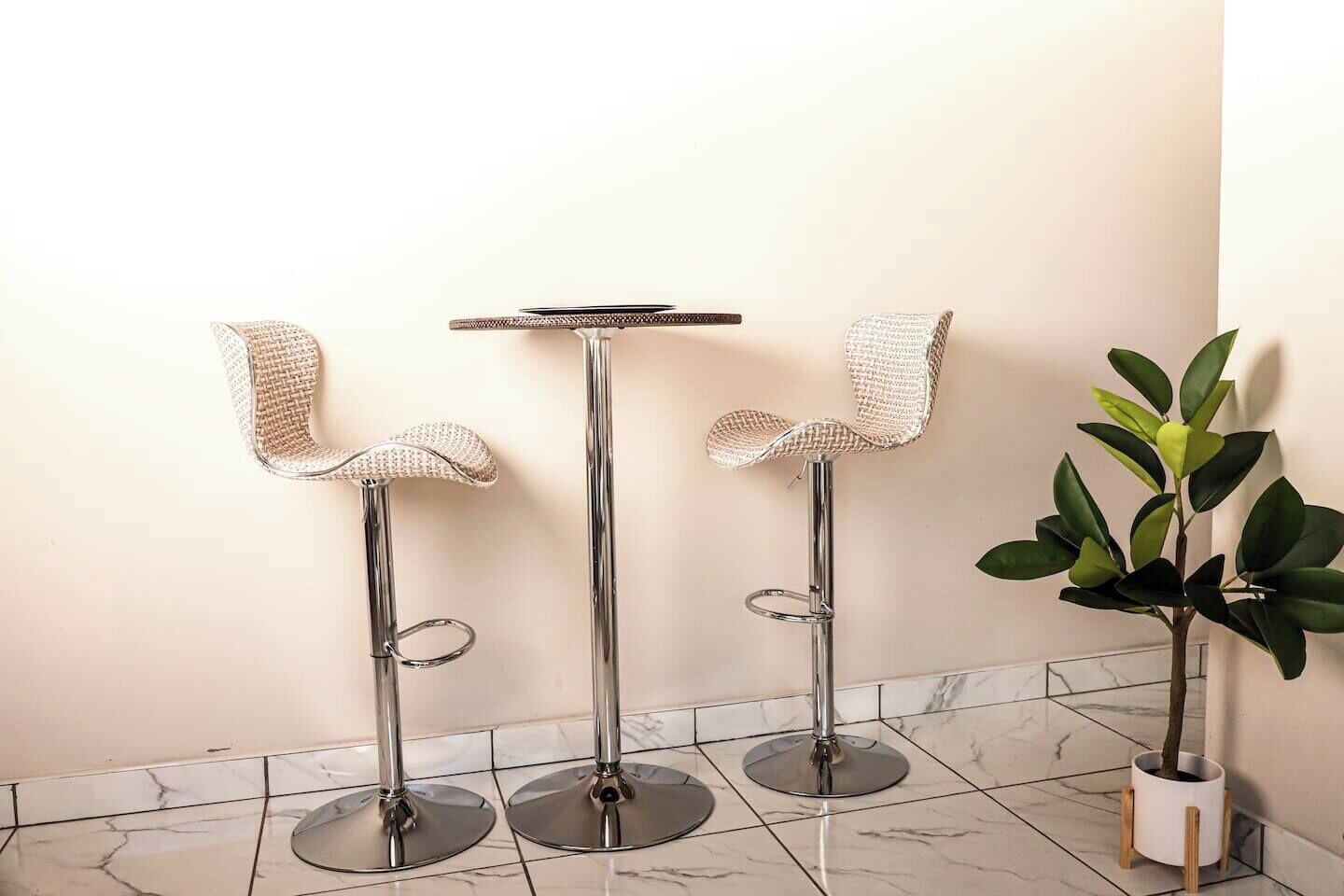 Drie barkrukken met geweven zittingen en metalen poten, een kleine ronde tafel en een potplant met groene bladeren.