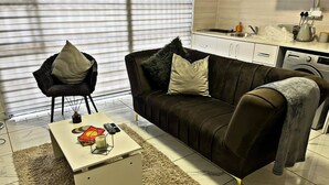 A living room with a sofa, a coffee table, a chair, and a kitchen area in the background. - Elite Luxury Garden Escape, Executive Cottage in Welkom with Wi-Fi & Parking (Welkom)