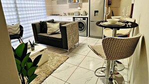 A compact living space with a sofa, dining table, and chairs, a washing machine, and a refrigerator. - Elite Luxury Garden Escape, Executive Cottage in Welkom with Wi-Fi & Parking (Welkom)