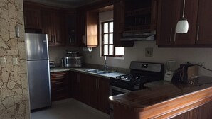 Une cuisine avec des meubles en bois, un réfrigérateur en acier inoxydable, un four à micro-ondes, une cuisinière et une fenêtre.