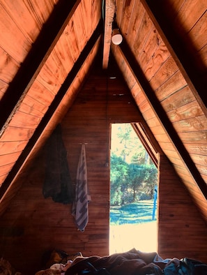 A wooden attic room with a slanted ceiling, a hanging towel, and a window with a view of greenery outside. - Camping Monte Verde  (Monte Verde)