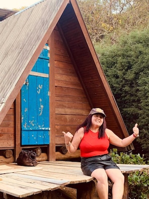 A woman sitting on a wooden deck with a wooden cabin in the background. - Camping Monte Verde  (Monte Verde)