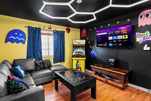 A living room with a sofa, coffee table, and a TV displaying a game interface.