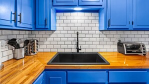 Eine Küche mit blauen Schränken, einem schwarzen Spülbecken, einem Toaster und einer weißen Fliesenwand.