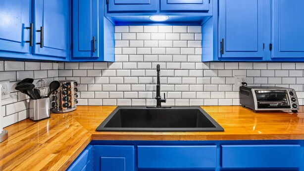Une cuisine avec des meubles bleus, un évier noir, un grille-pain et un dosseret de carrelage blanc.