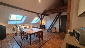 A loft-style room with a wooden dining table, chairs, a large window, and a skylight.