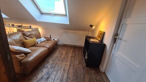 Een knus vertrek met een bruine leren bank, een klein wit nachtkastje, een radiator en een zwarte kast.