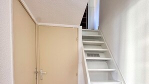 Una escalera con escalones blancos que conducen a un piso superior, una puerta cerrada con manija y un suelo de madera.