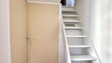 A staircase with white steps leading to an upper floor, a closed door with a handle, and a wooden floor.