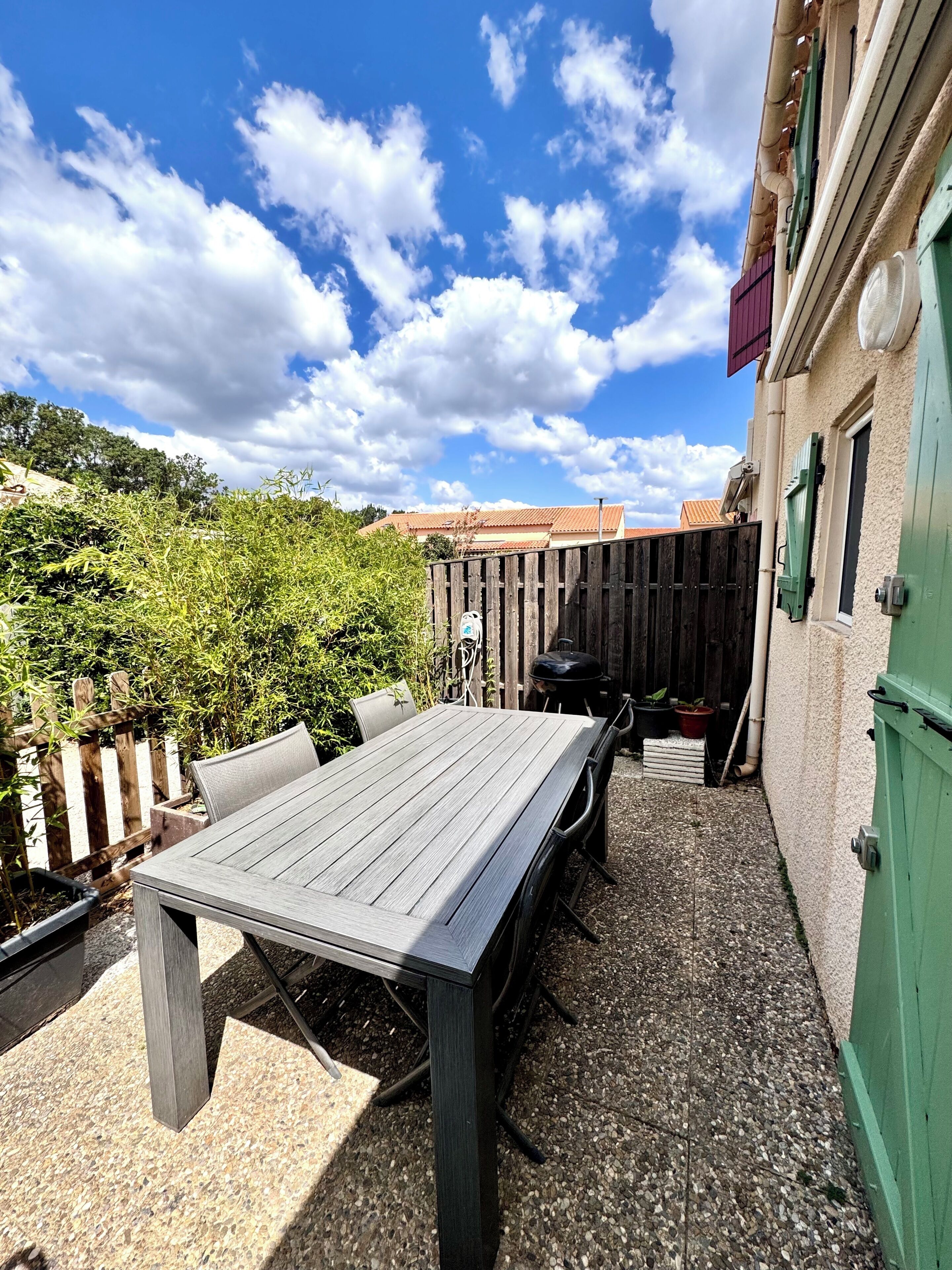 A patio with a table and chairs, a wooden fence, and a building with a green door.