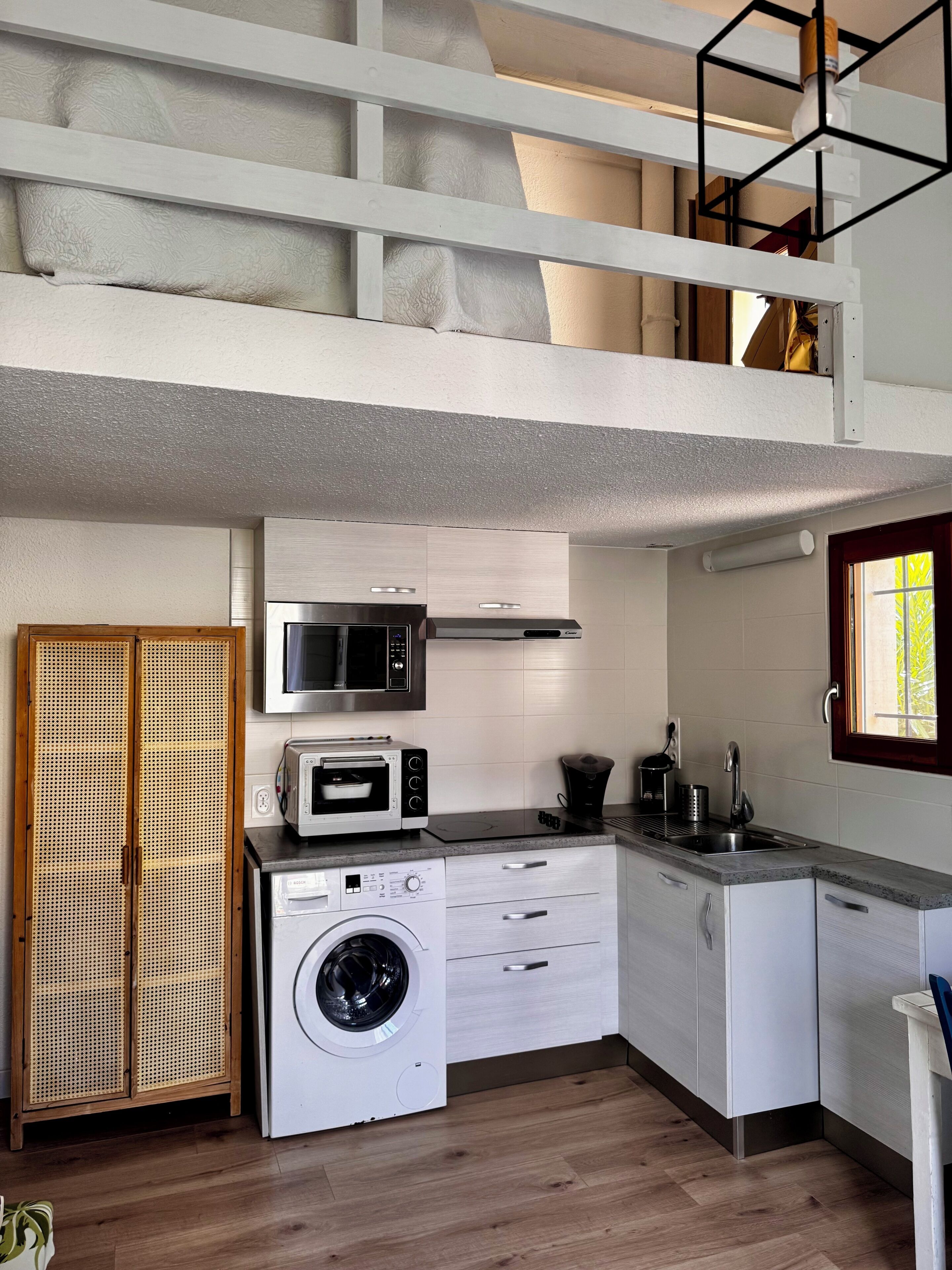 Een functionele keuken met een wasmachine, magnetron en een klein spoelgedeelte.
