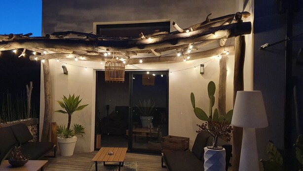 En udendørs terrasse med lysslinger, træmøbler og plantekasser.