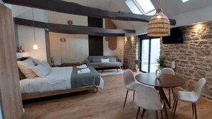 A modern interior with a bed, sofa, dining table, and chairs. - Le Clos de Squividan - L'Évasion (Ergué-Gabéric)