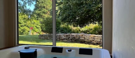 A hot tub with a stone wall and greenery outside.