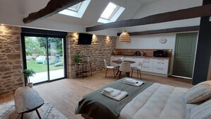 A bedroom with a large bed, a sitting area with a chair, a small table, and a kitchen area with a dining table and chairs. - Le Clos de Squividan - L'Évasion (Ergué-Gabéric)