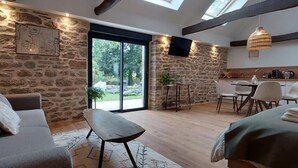A modern interior with a stone wall, a sofa, a dining area, and a large sliding glass door leading to a garden. - Le Clos de Squividan - L'Évasion (Ergué-Gabéric)