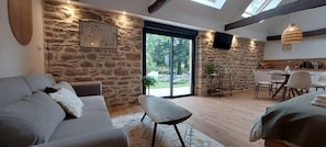 Um interior moderno com parede de pedra, sofá, área de jantar e uma grande porta de correr de vidro que dá para um jardim.