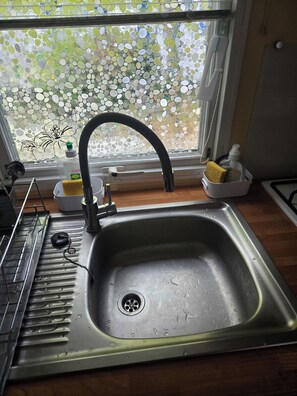 Eine Küche mit einer Edelstahl-Spüle, einem Geschirrgestell und einem Fenster mit Mosaikmuster.