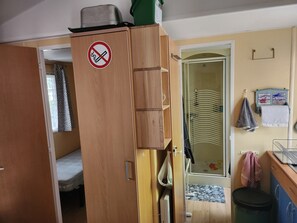 Ein Zimmer mit Holzschrank, einem Rauchverbot-Hinweis, einem Badezimmer mit Handtuchhalter und einer kleinen Mülltonne.