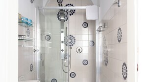 Casa de banho com chuveiro em cabine de vidro, lavatório branco e azulejos decorativos.