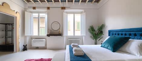 A bedroom with a bed, a radiator, a window, a plant, and a ceiling with a sun design.