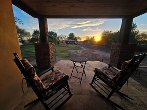 Ulkoterassi, jossa on kaksi keinutuolia, pieni pöytä ja näkymä auringonlaskuun, joka heijastuu maantieltä.