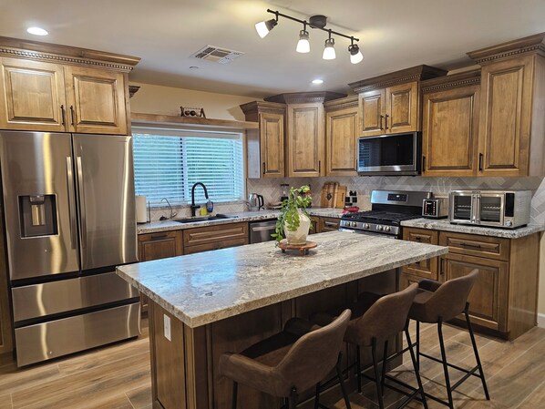 A kitchen with wooden cabinets, stainless steel appliances, a granite countertop, and bar stools.