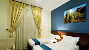 Ein Hotelzimmer mit zwei Betten, einem Sessel, einem Nachttisch mit Lampe und einem großen Wandbild einer Säulenkaktus.