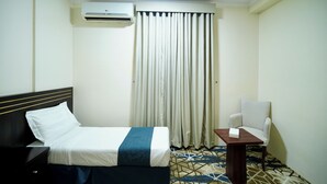 Ein Hotelzimmer mit Bett, Sessel, kleinem Tisch, Klimaanlage und einem Vorhangfenster.