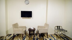 Ein Zimmer mit zwei Sesseln, einem kleinen Tisch mit Fernbedienung, einem an der Wand befestigten Fernseher und einer Uhr.