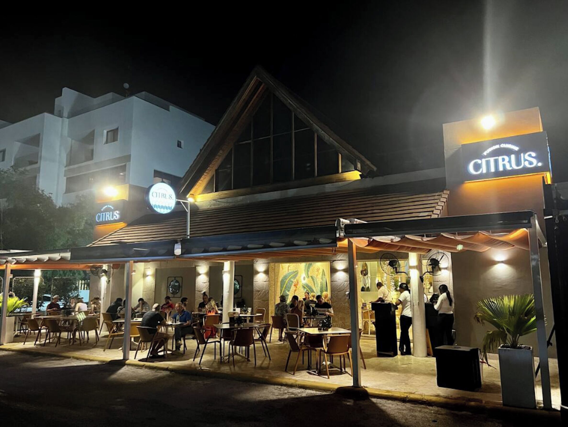 An outdoor seating area of a restaurant with tables and chairs, a covered section, and a sign for 'CITRUS.'