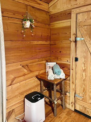 Ein Zimmer mit Holzboden und einer Holztür, ein kleiner Tisch mit Handtüchern, ein weißer Heizkörper und eine hängende Pflanze.
