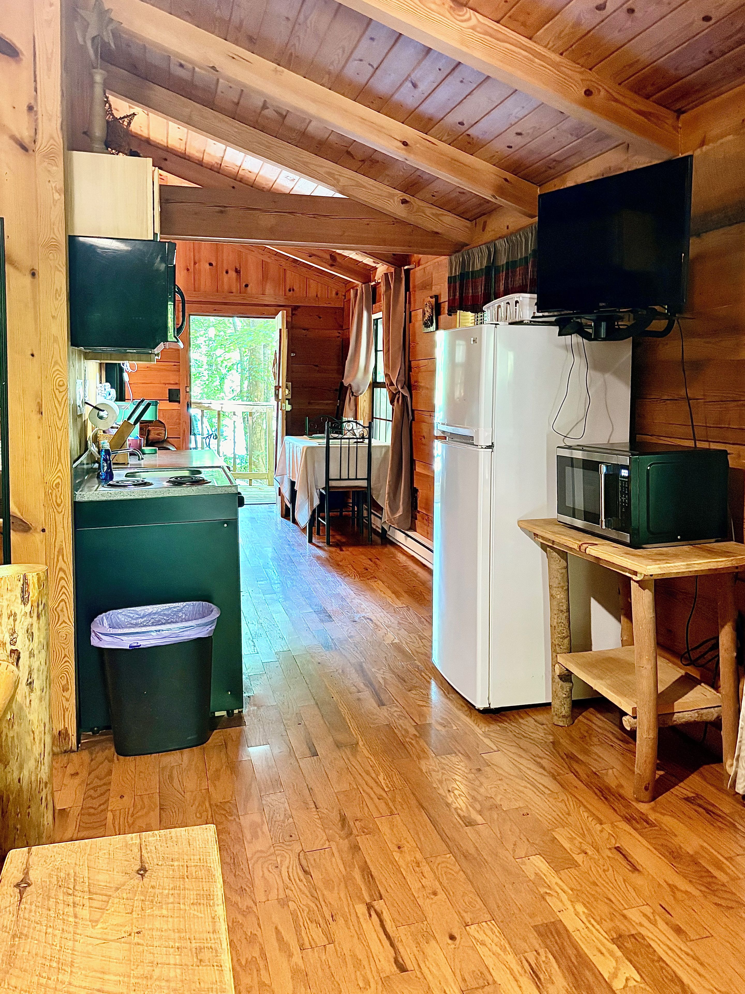 A wooden cabin interior with a kitchen area featuring a refrigerator, microwave, and a dining table with chairs.