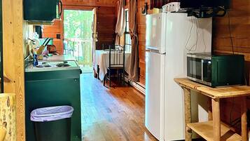 A wooden cabin interior with a kitchen area featuring a refrigerator, microwave, and a dining table with chairs.