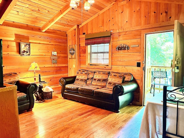 L’intérieur d’une cabane est doté d’un plancher en bois, d’un canapé en cuir, d’une table avec une lampe et d’une fenêtre avec des stores.