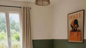 Ein Schlafzimmer mit Bett, Nachttisch, Lampe, einem Fenster mit Vorhängen und einem an der Wand hängenden Poster.
