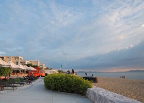 Eine Strandpromenade mit Liegestühlen, einem roten Fahrzeug und einer Steinmauer.
