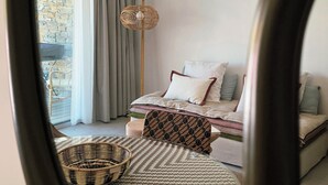 Un dormitorio con cama, lámpara colgante, silla de mimbre y vista por la ventana.